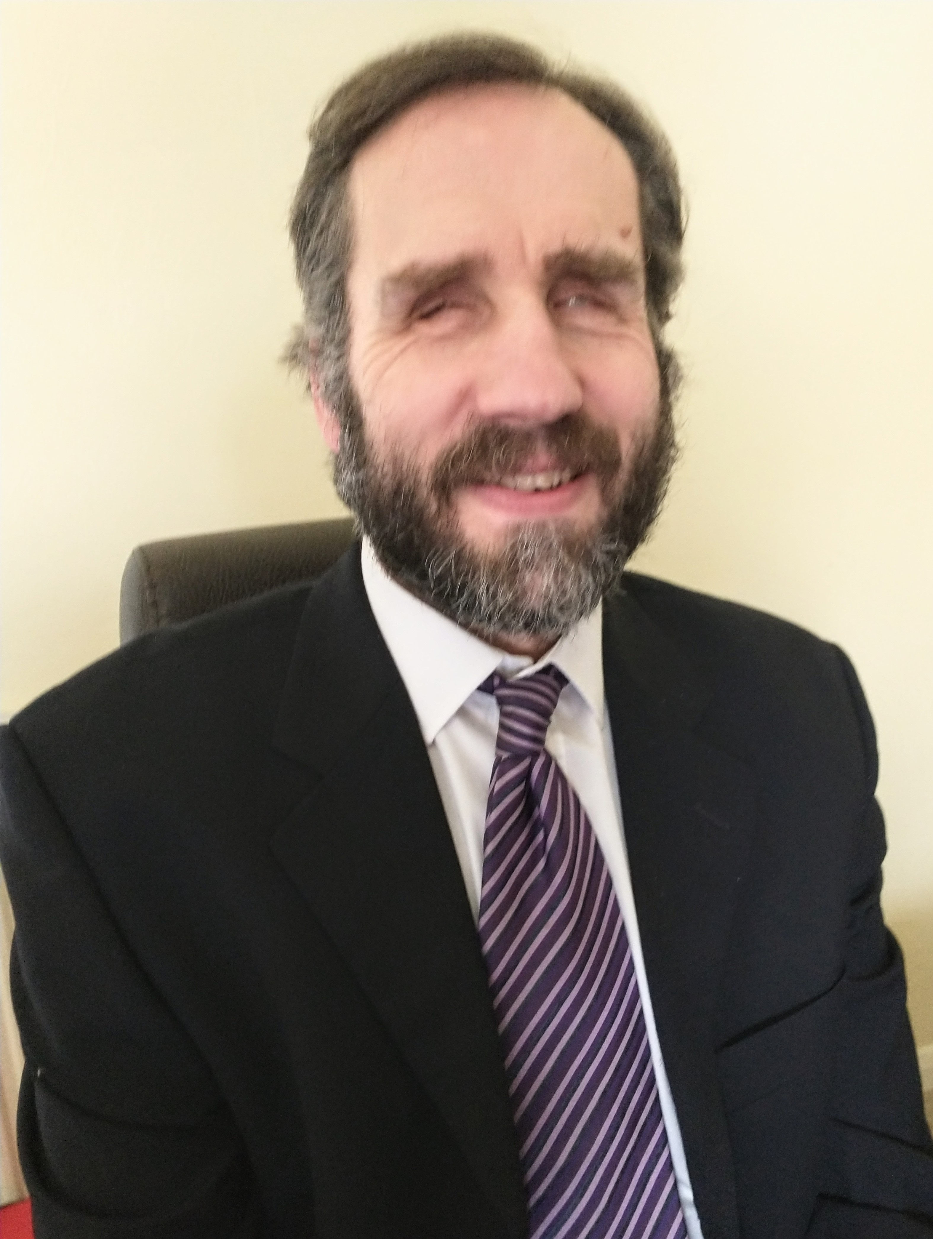 Photo of Martin Fleming, founder of Spectrom, he has a beard, is wearing a dark suit, and a white shirt paired with a striped tie. He has a gentle smile and the overall appearance is professional.